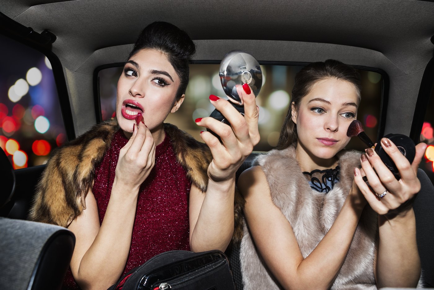Zwei junge Frauen schminken sich auf dem Rücksitz eines Autos
